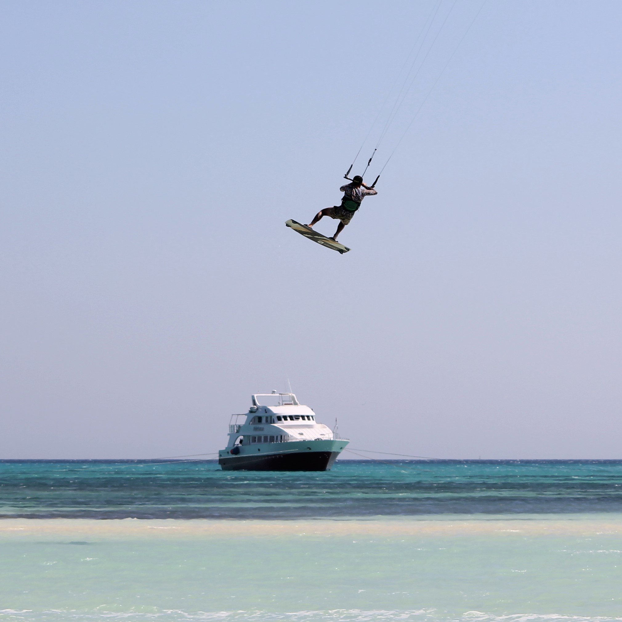 Kite cruise Egypt. A kitesurfer performs a trick in air. A cruise yacht is anchored